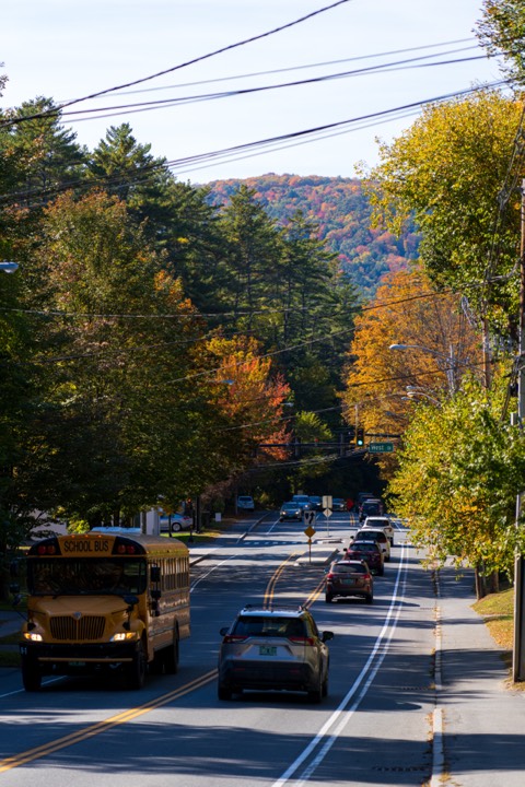 Town street in fall, a school bus rounding the bend