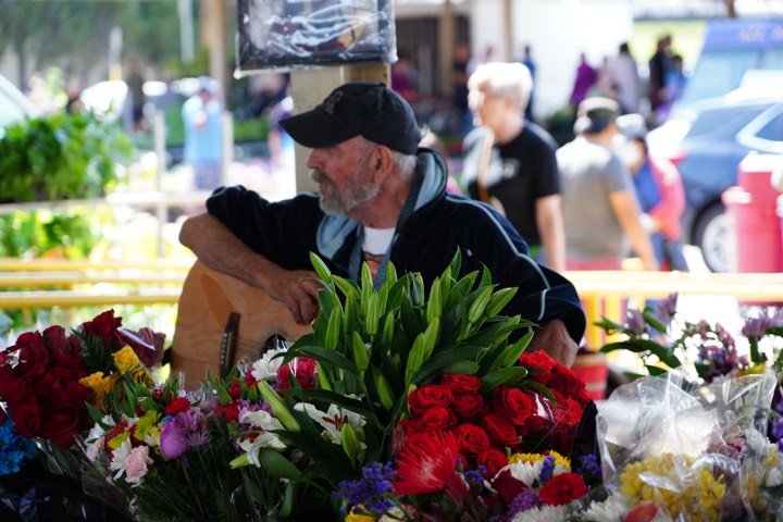 A man resting with his guitar at a flower market