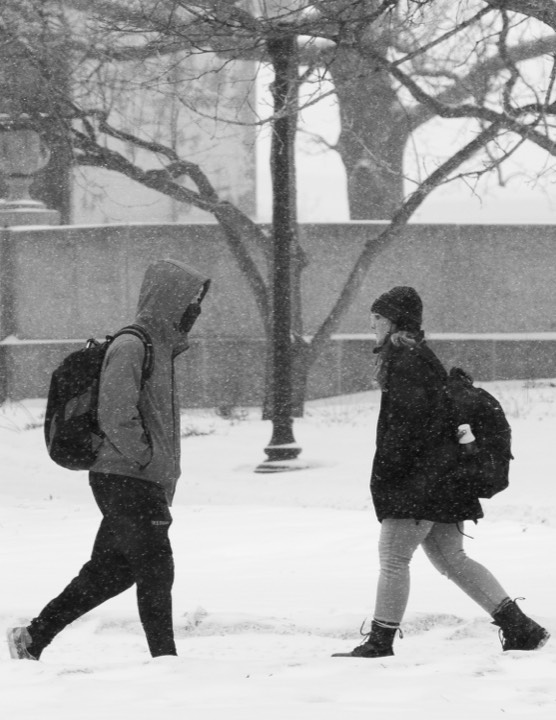 Two students crossing campus through falling snow
