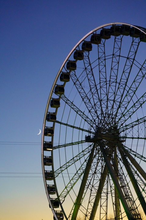 Ferris wheel and a crescent moon against deep blue dusk